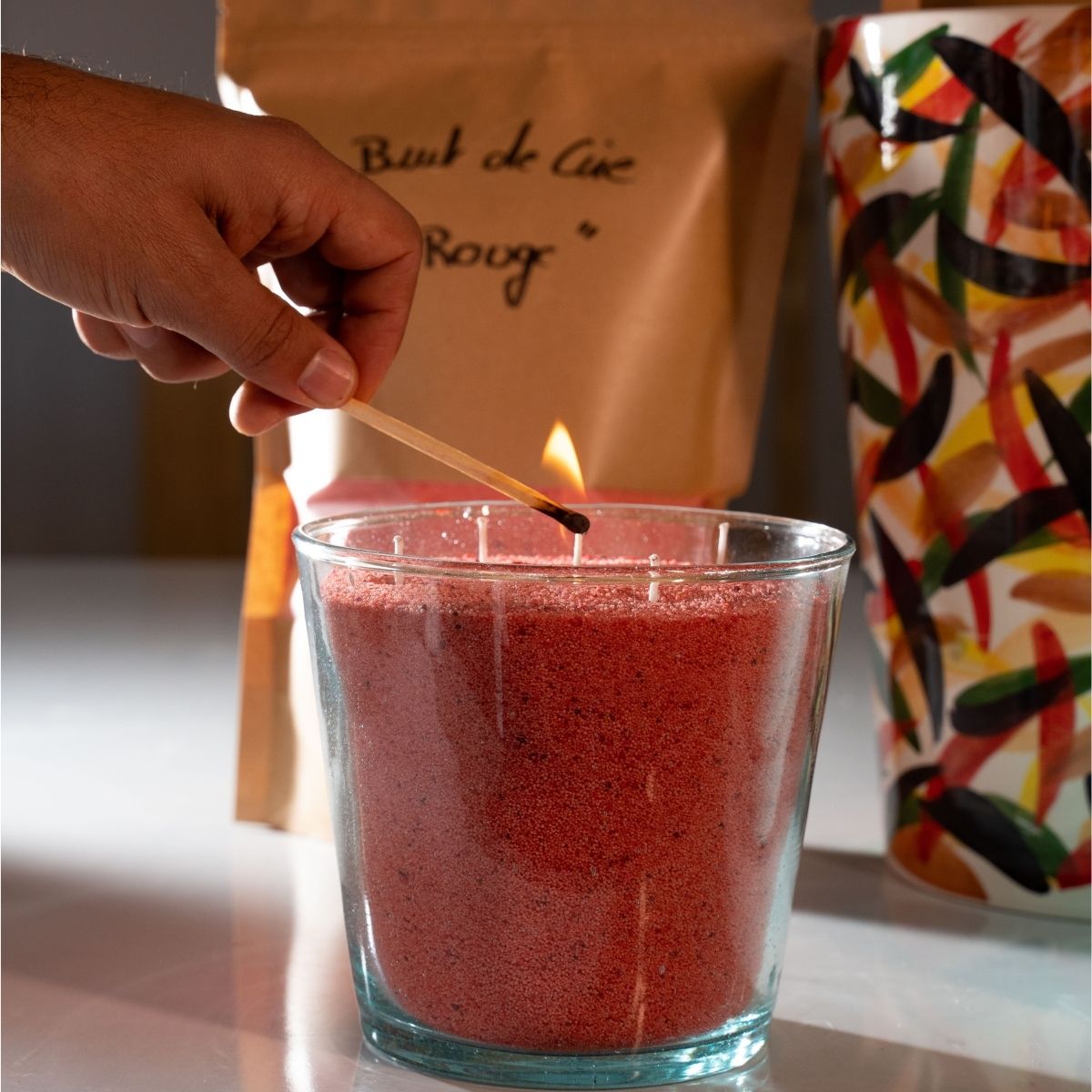 A lit match ignites the red sand wax candle in a handcrafted glass vessel — a moment where handmade artisanal craftsmanship harmonizes with warm, sustainable luxury. This scene showcases Dary Living’s refined candle-making process and striking, elegant color choice. Every detail reflects Dary Living’s dedication to timeless artistry and meticulous care, where each element is crafted with intention, elegance, and sustainability. Through a mindful, handmade approach, Dary Living merges skilled technique with 