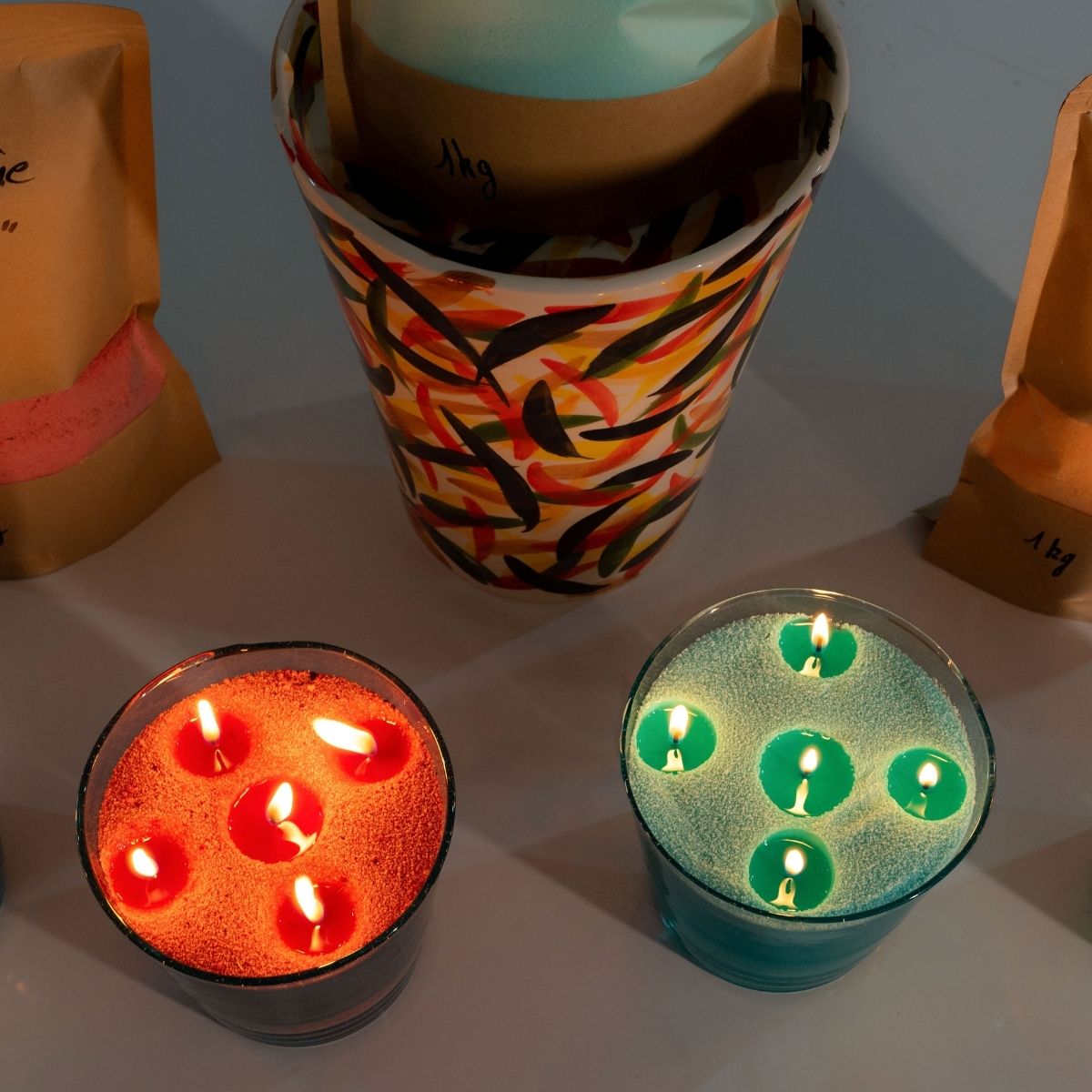 Two handcrafted, handmade glass vessels glow warmly — one filled with vibrant green sand wax, the other with warm orange sand wax. Both candles are ignited to illuminate elegant, serene spaces, showcasing Dary Living’s artisanal craftsmanship and rich, colorful wax for a refined home ambiance.
